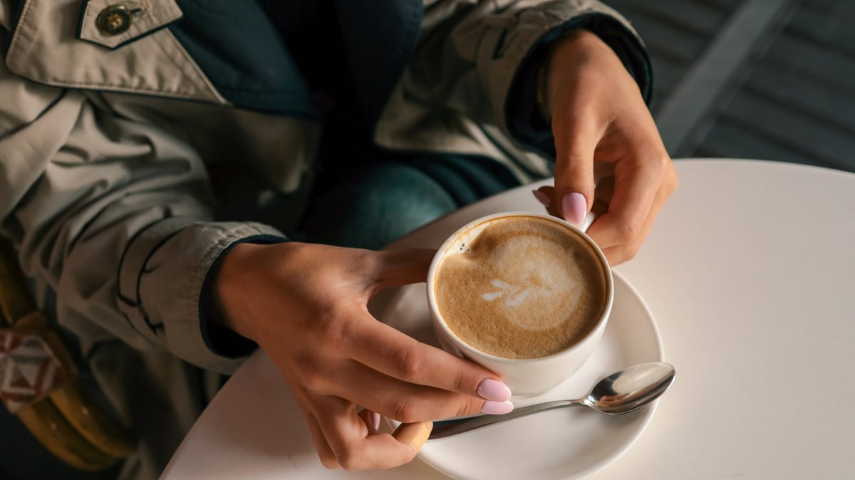 Hands holding a cappuccino with latte art in a cozy outdoor café